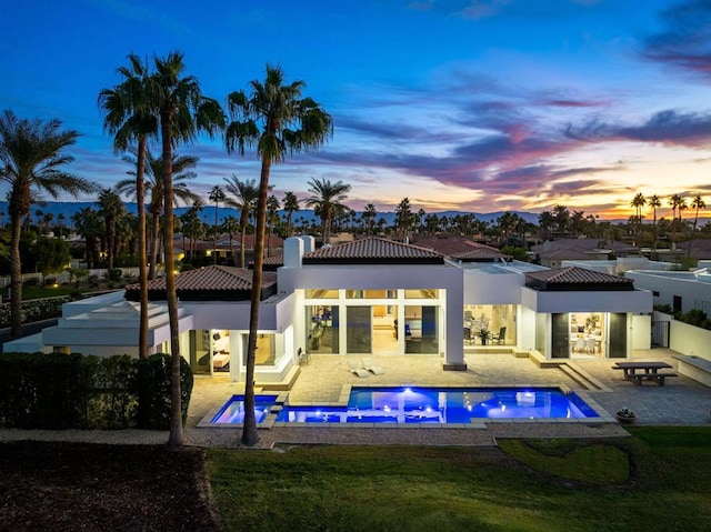 back house at dusk with a patio area and a pool with hot tub