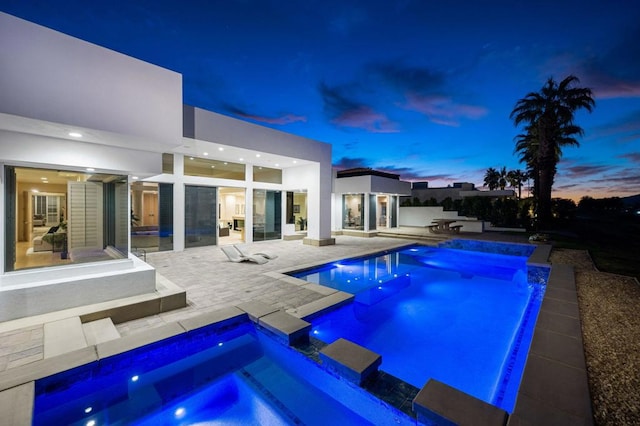 pool at dusk featuring pool water feature, an in ground hot tub, and a patio