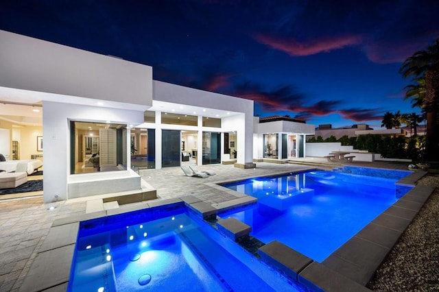 pool at dusk with an in ground hot tub and a patio