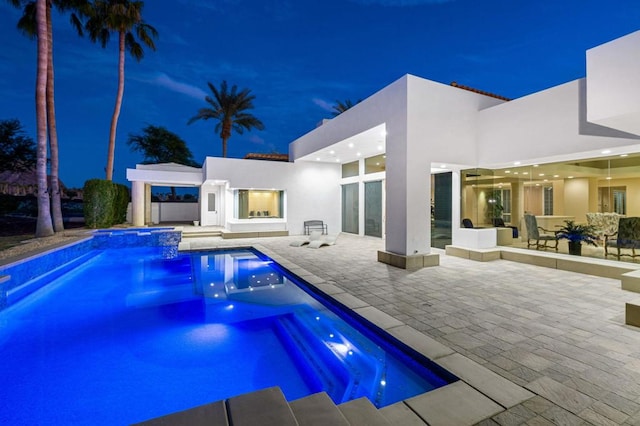 pool at night featuring an in ground hot tub and a patio