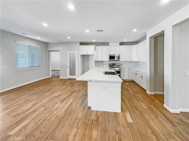 kitchen with white cabinetry, appliances with stainless steel finishes, a kitchen island with sink, and light hardwood / wood-style floors