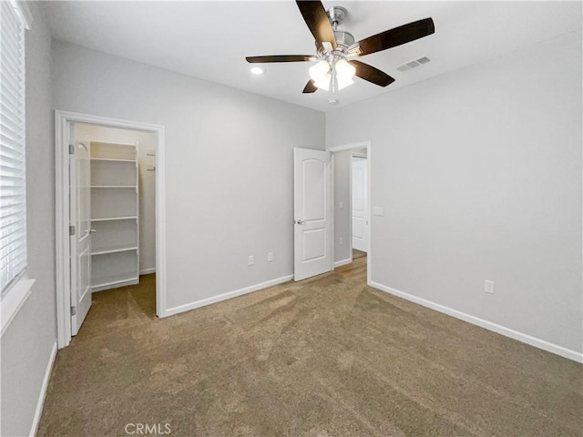 unfurnished bedroom with a spacious closet, a closet, ceiling fan, and carpet