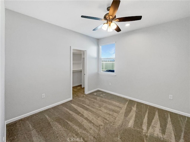 unfurnished bedroom with a walk in closet, a closet, ceiling fan, and carpet