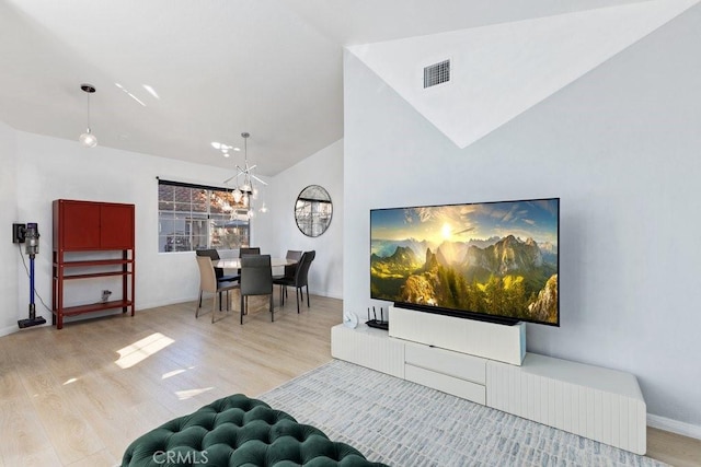 living room with vaulted ceiling, an inviting chandelier, and light wood-type flooring