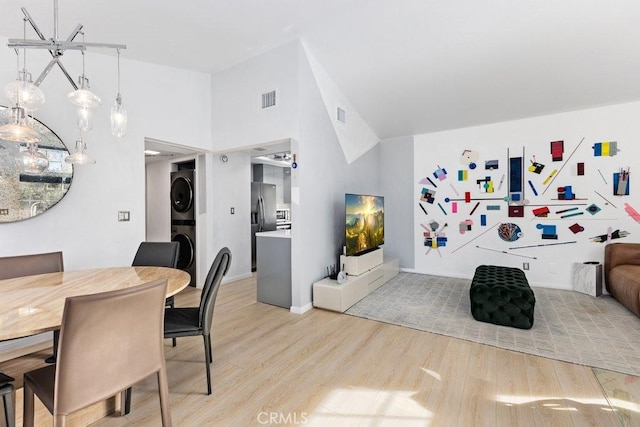 interior space featuring stacked washer / drying machine, lofted ceiling, a notable chandelier, and light hardwood / wood-style flooring