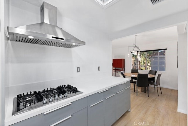 kitchen featuring exhaust hood, hanging light fixtures, gray cabinets, a chandelier, and stainless steel gas stovetop