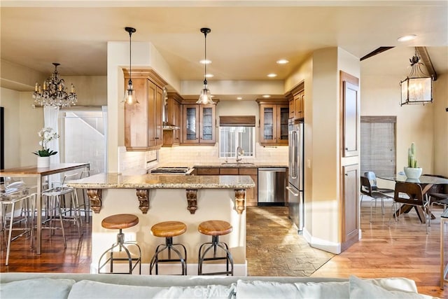 kitchen with appliances with stainless steel finishes, hanging light fixtures, kitchen peninsula, sink, and backsplash