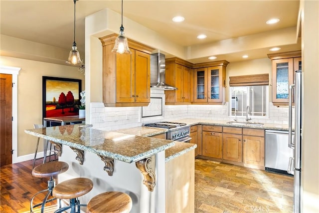 kitchen with sink, high end appliances, light stone counters, and wall chimney exhaust hood