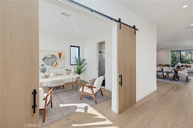 hall featuring a barn door, light hardwood / wood-style flooring, and a healthy amount of sunlight