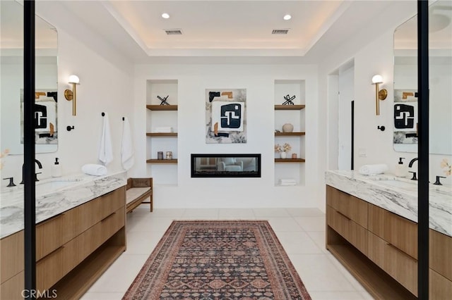 bathroom with a tray ceiling, built in shelves, and vanity