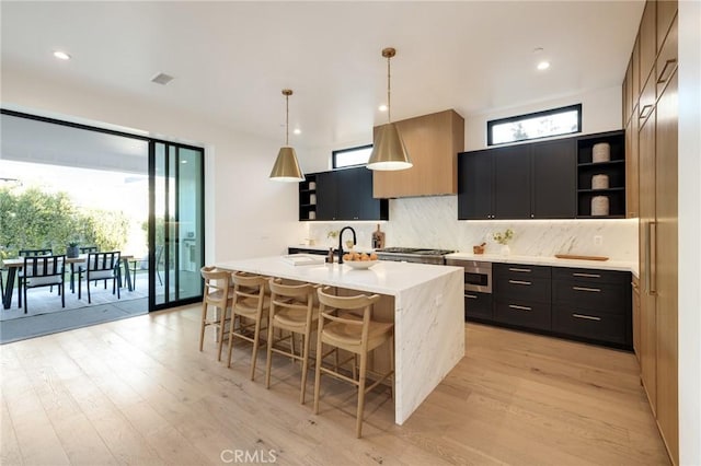 kitchen featuring a center island with sink, appliances with stainless steel finishes, hanging light fixtures, and light wood-type flooring