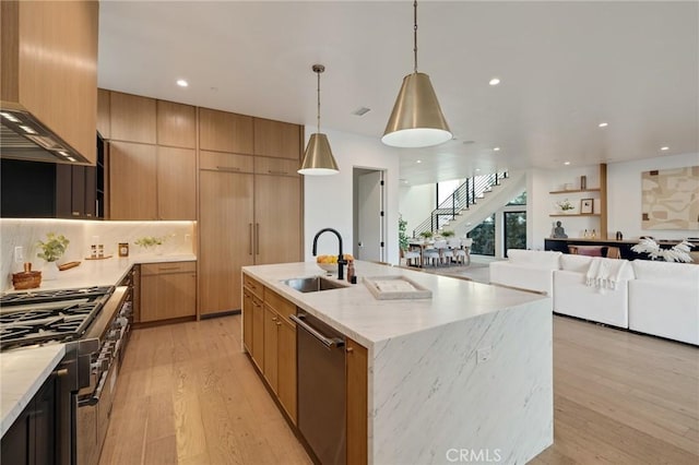 kitchen with sink, decorative light fixtures, a center island with sink, appliances with stainless steel finishes, and light wood-type flooring