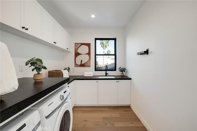 laundry room featuring washing machine and clothes dryer, light hardwood / wood-style floors, cabinets, and sink