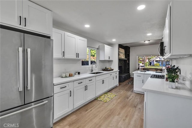 kitchen with sink, white cabinets, light wood-type flooring, and stainless steel fridge