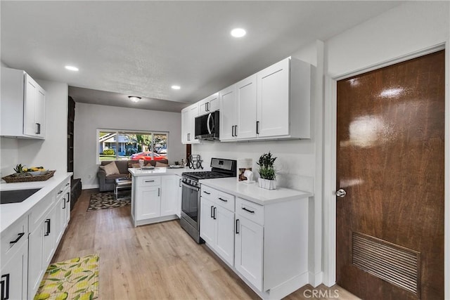 kitchen featuring sink, white cabinets, light wood-type flooring, kitchen peninsula, and gas stove