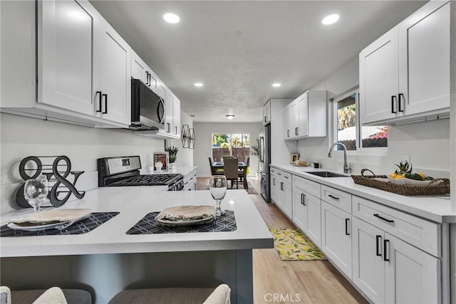 kitchen featuring stainless steel appliances, a breakfast bar, white cabinets, light hardwood / wood-style flooring, and sink