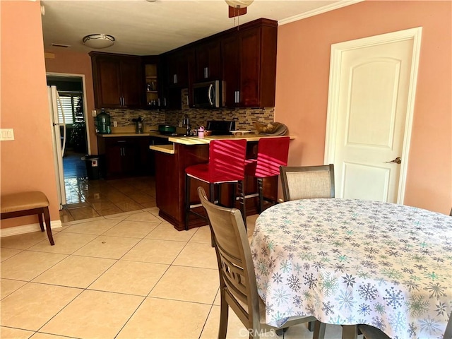 kitchen with a kitchen bar, decorative backsplash, kitchen peninsula, ornamental molding, and light tile patterned floors