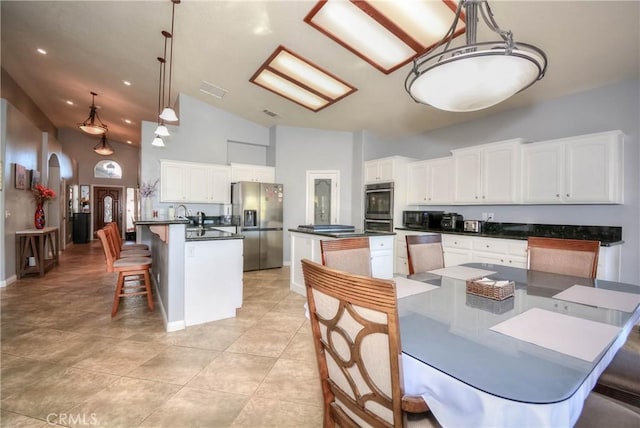 kitchen with a kitchen island, high vaulted ceiling, decorative light fixtures, white cabinets, and appliances with stainless steel finishes