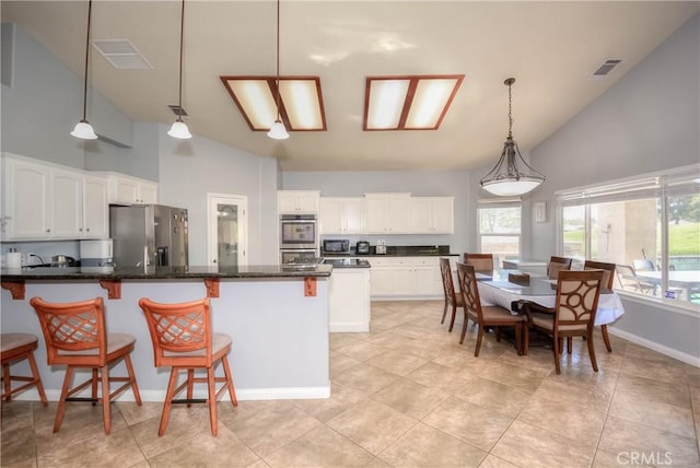 kitchen with high vaulted ceiling, dark stone countertops, pendant lighting, white cabinets, and appliances with stainless steel finishes