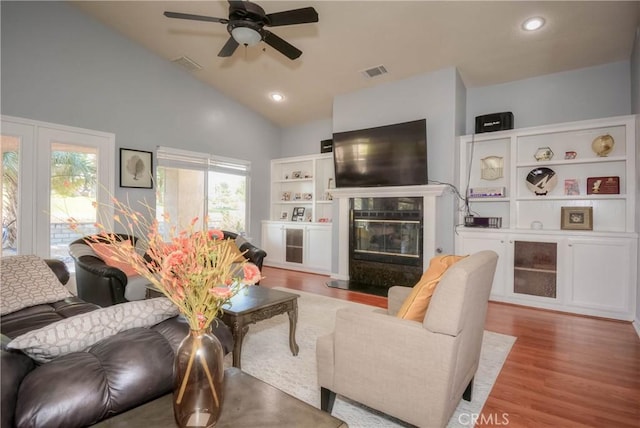 living room with a premium fireplace, ceiling fan, high vaulted ceiling, and light wood-type flooring