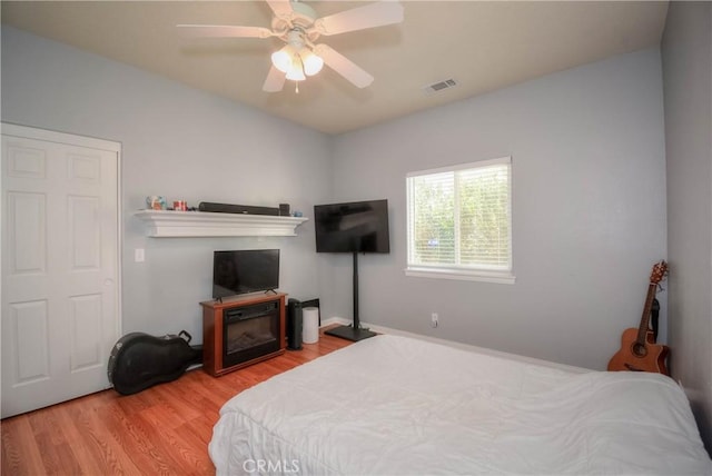 bedroom with a fireplace, light wood-type flooring, and ceiling fan