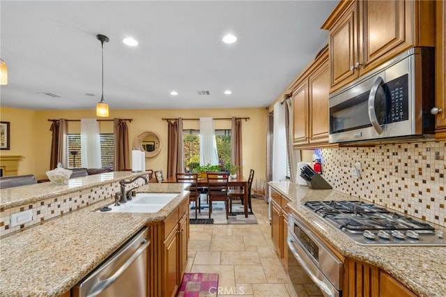 kitchen featuring light stone countertops, backsplash, stainless steel appliances, sink, and decorative light fixtures