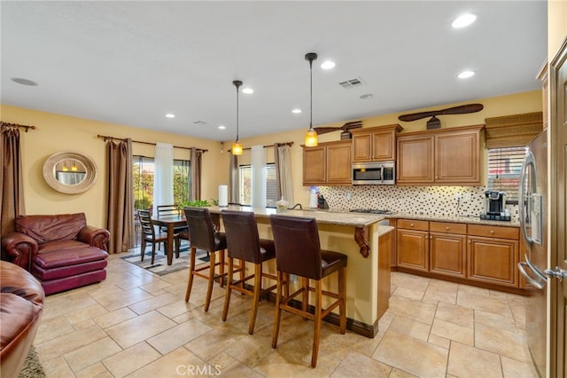 kitchen with pendant lighting, a kitchen island with sink, decorative backsplash, appliances with stainless steel finishes, and a kitchen bar