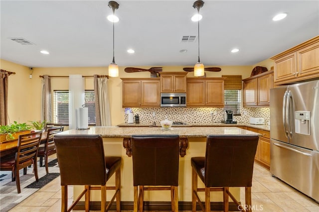 kitchen with light stone countertops, appliances with stainless steel finishes, a breakfast bar, a kitchen island, and hanging light fixtures