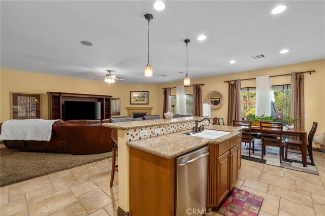 kitchen featuring sink, stainless steel dishwasher, decorative light fixtures, a kitchen bar, and a center island with sink