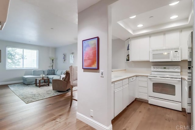 kitchen featuring a raised ceiling, white appliances, light hardwood / wood-style floors, and white cabinetry