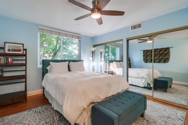 bedroom with ceiling fan, hardwood / wood-style floors, and two closets