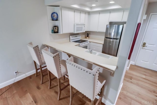 kitchen with white cabinets, light hardwood / wood-style floors, white appliances, and a tray ceiling