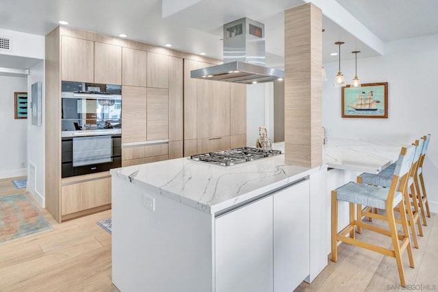 kitchen with pendant lighting, stainless steel gas stovetop, light stone countertops, light wood-type flooring, and island exhaust hood