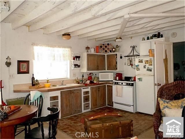 kitchen featuring beam ceiling, sink, and white appliances