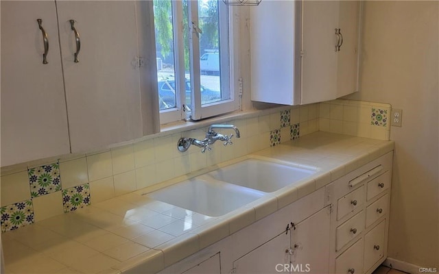 kitchen with decorative backsplash, tile counters, white cabinets, and sink