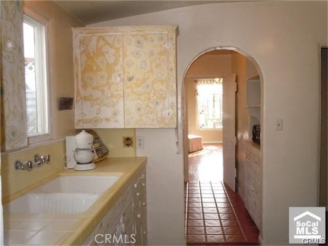 bathroom featuring tile patterned flooring, lofted ceiling, a healthy amount of sunlight, and sink