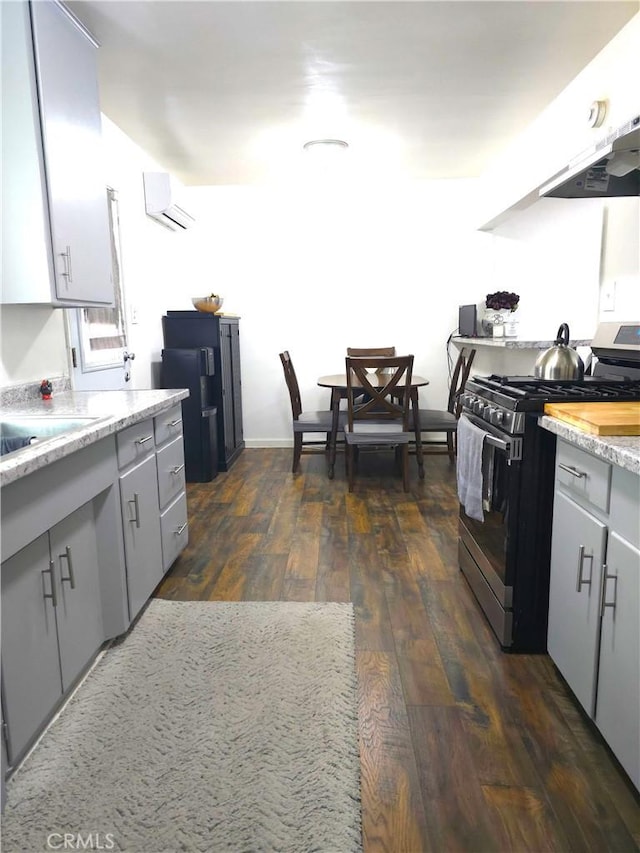 kitchen featuring stainless steel range with gas cooktop, dark hardwood / wood-style floors, a wall mounted AC, extractor fan, and gray cabinets