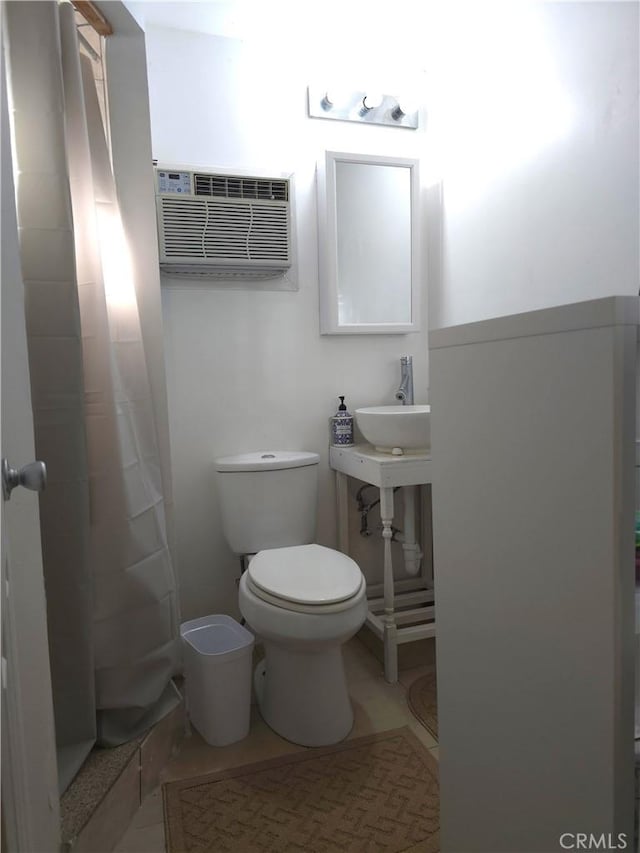 bathroom with tile patterned floors, walk in shower, a wall mounted AC, sink, and toilet