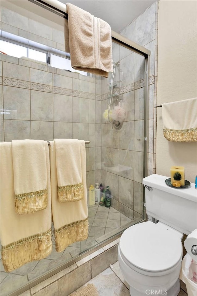 bathroom featuring tile patterned flooring, toilet, and a shower with shower door