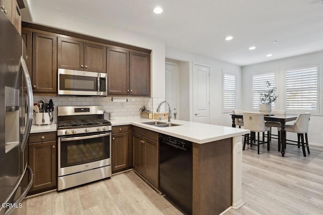 kitchen with kitchen peninsula, sink, light hardwood / wood-style floors, and appliances with stainless steel finishes