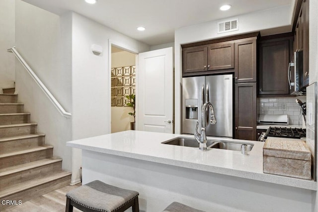 kitchen featuring sink, stainless steel appliances, tasteful backsplash, light hardwood / wood-style floors, and a breakfast bar