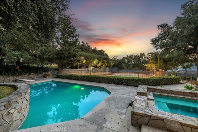 pool at dusk with a diving board and an in ground hot tub