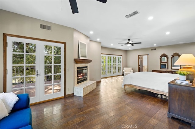 bedroom featuring ceiling fan, dark hardwood / wood-style floors, a tiled fireplace, access to outside, and french doors