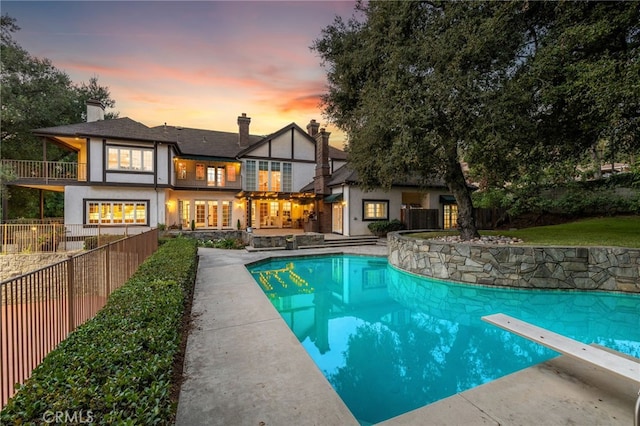 pool at dusk featuring a patio area and a diving board