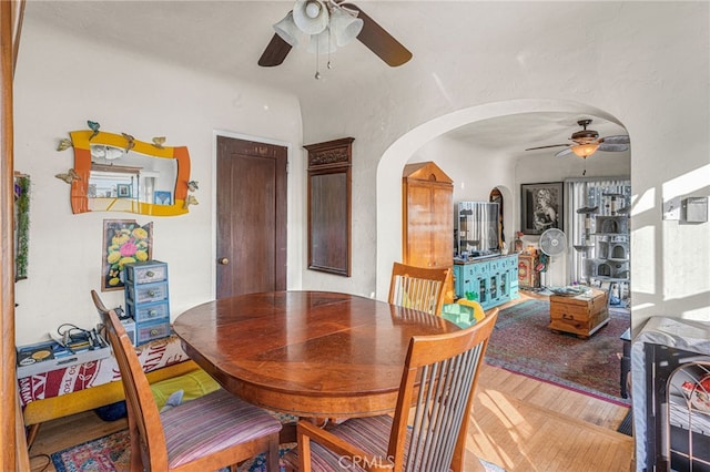 dining space featuring ceiling fan, arched walkways, and wood finished floors