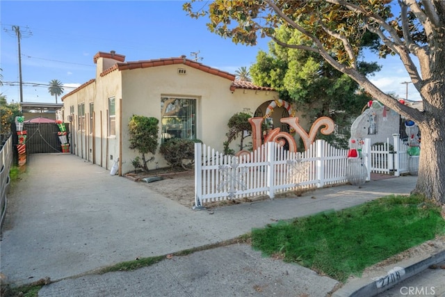 mediterranean / spanish-style house with a tile roof, stucco siding, a gate, and a fenced front yard