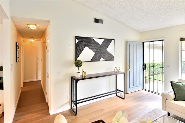 foyer entrance with a textured ceiling, light hardwood / wood-style flooring, and vaulted ceiling