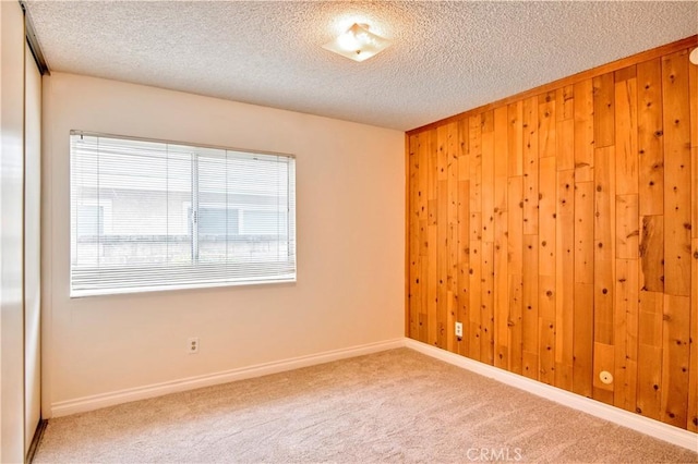 carpeted empty room featuring wooden walls and a textured ceiling