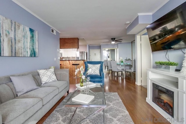 living room featuring ceiling fan, ornamental molding, and dark hardwood / wood-style floors