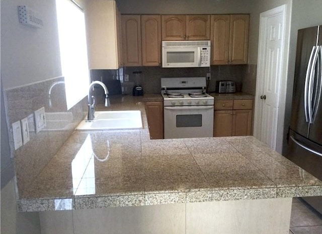 kitchen with sink, backsplash, kitchen peninsula, white appliances, and light brown cabinetry